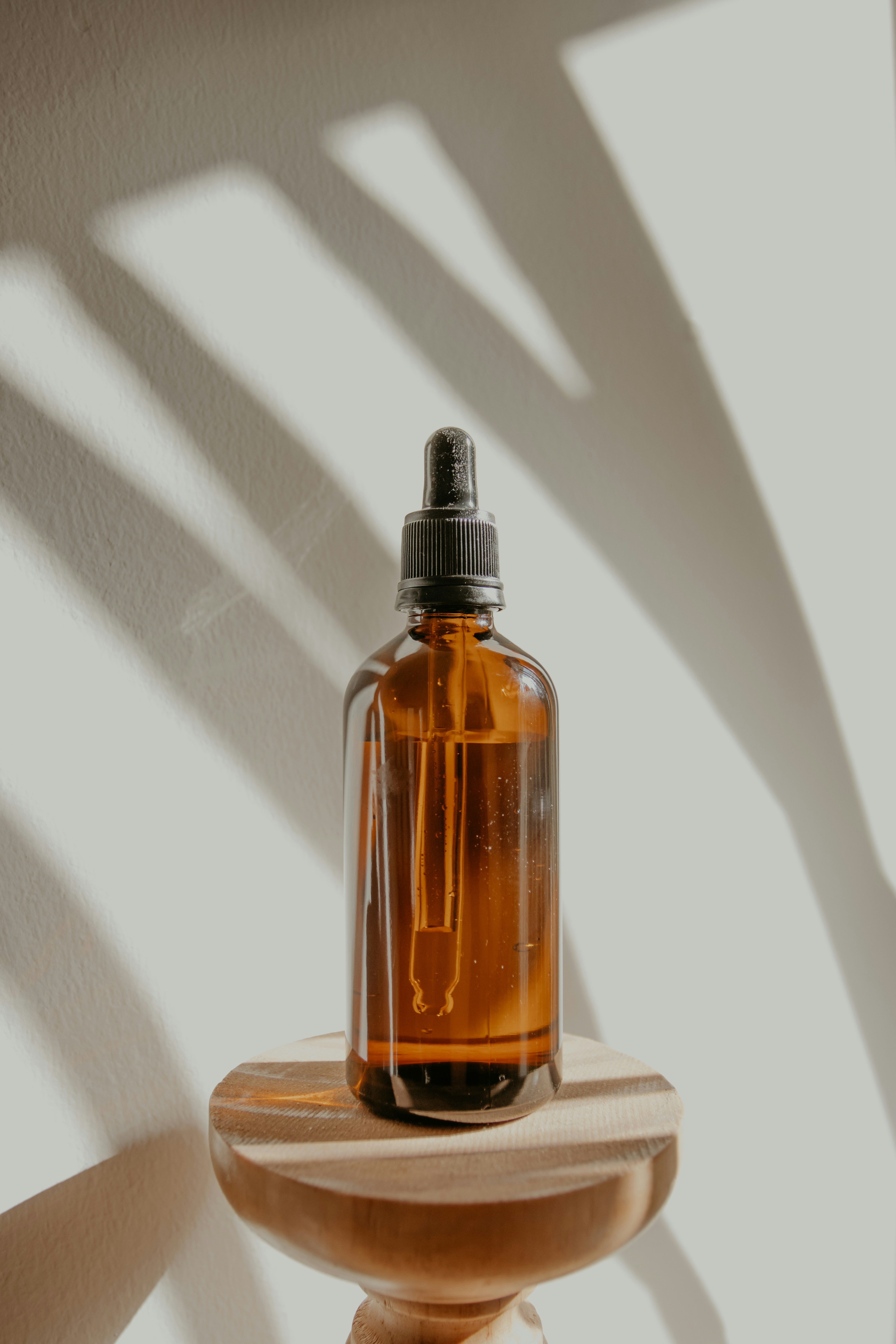 Amber dropper bottle on a wooden stand with soft palm shadows